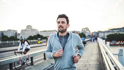 Junger Mann joggt auf einer Brücke in der Stadt mit Kopfhörern im Ohr Junger Mann joggt auf einer Brücke in der Stadt mit Kopfhörern im Ohr