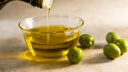 Closeup einer kleinen Glasschale, in die Olivenöl gegossen wird, neben der Schale liegen ein paar Oliven