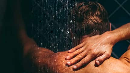 Mann steht unter der Dusche und wäscht sich den Rücken.