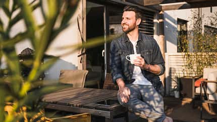 Mann sitzt draußen auf der sonnigen Terrasse mit einer Tasse in der Hand