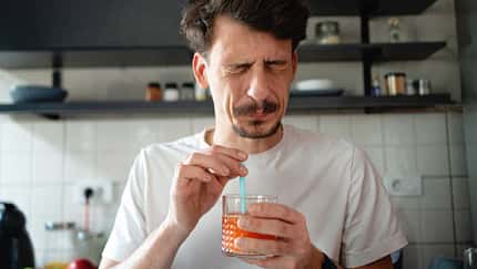 Mann in weißem T-Shirt hält einen frischen Saft in der Hand und verzieht sein Gesicht