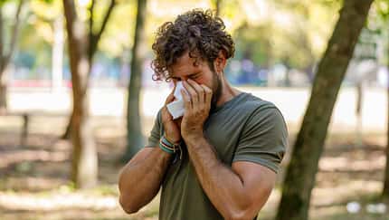 Ein Mann im T-Shirt steht im Park und niest in ein Taschentuch