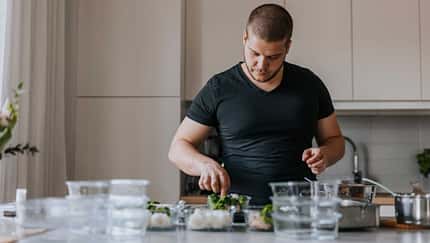 Mann im T-Shirt steht in seiner Küche und bereitet sich einen Snack zu