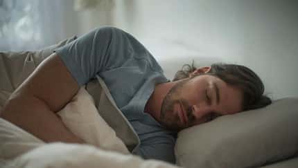 Ein junger Mann schläft zugedeckt in einem Bett