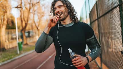 Mann in Sportkleidung geht draußen auf einer Laufstrecke und isst einen Proteinriegel