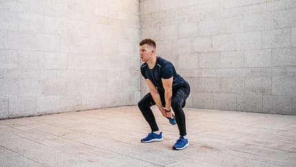 Sportlicher Mann in leerem Raum führt eine Hip Hinge Übung mit einem Kettle Ball aus