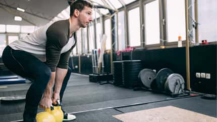 Mann führt in einem Fitnessstudio eine Squatbewegung mit Kettleballs aus