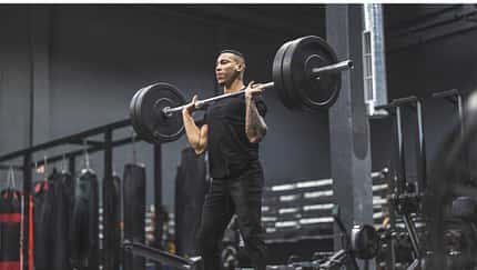 Ein Mann steht im Fitnessstudio und stemmt eine Langhantel Ein Mann steht im Fitnessstudio und stemmt eine Langhantel