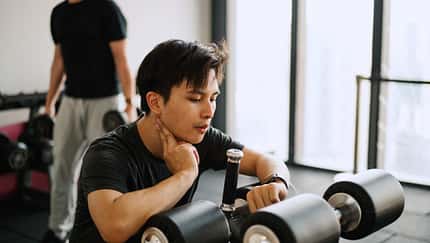 Asiatisch stämmiger Mann sitzt auf einem Fitnessgerät und checkt seinen Ruhepuls auf seiner Smartwatch