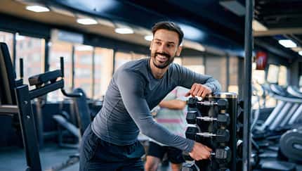 Junger Mann, der Hanteln für sein Training im Fitnessstudio auswählt Junger Mann, der Hanteln für sein Training im Fitnessstudio auswählt