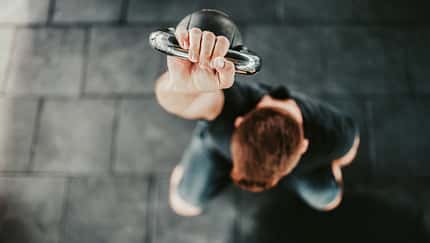 Junger Mann hält eine Kettlebell über seinem Kopf