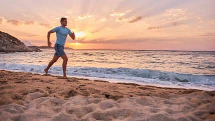 Ein sportlicher Mann läuft am Strand während im Hintergrund die Sonne untergeht
