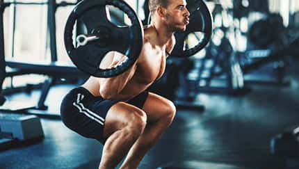 Sportlicher Mann macht oberkörperfrei eine Squatübung mit einer Langhantel im Fitnessstudio