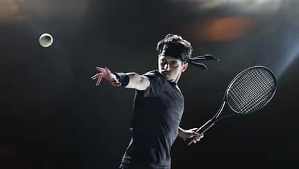 Tennisspieler in schwarzem Outfit wirft einen Tennisball und holt mit dem Schläger aus Tennisspieler in schwarzem Outfit wirft einen Tennisball und holt mit dem Schläger aus
