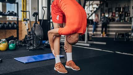Ein junger Mann in orangener Sportkleidung dehnt sich vor dem Training im Fitnessstudio.