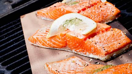Lachsfilets mit Zitronenscheiben garniert, auf einem Backpapier auf dem Grill Lachsfilets mit Zitronenscheiben garniert, auf einem Backpapier auf dem Grill