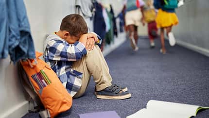 Ein Kind hockt traurig auf dem Flur vor seinem Klassenzimmer