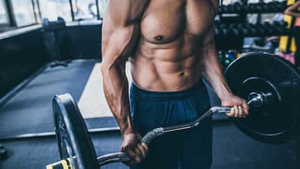 Muskulöser Mann trainiert mit Langhantel im Fitnessstudio Muskulöser Mann trainiert mit Langhantel im Fitnessstudio