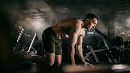 Ein Mann kniet oberkörperfrei auf dem Boden eines Fitnessstudios