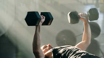 Mann trainiert im Fitnessstudio mit Hanteln und liegt auf der Hantelbank Mann trainiert im Fitnessstudio mit Hanteln und liegt auf der Hantelbank