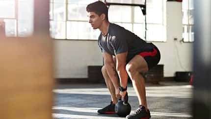 Mann macht eine Kniebeuge mit einem Kettleball