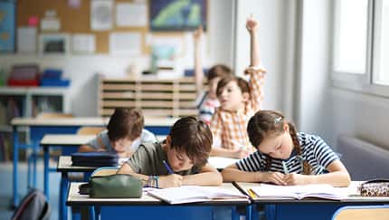 Blick in ein Klassenzimmer, Schüler sitzen an Tischen, einer meldet sich