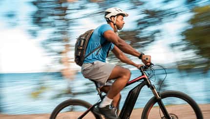 Ein Mann mittleren Alters fährt mit einem E-Bike am Meer entlang. Ein Mann mittleren Alters fährt mit einem E-Bike am Meer entlang.
