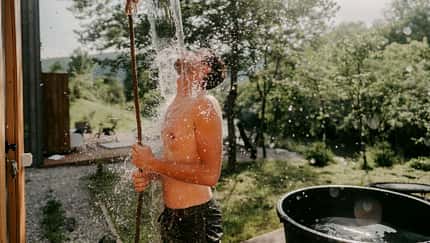 Ein Mann nimmt draußen oberkörperfrei eine Eisdusche Ein Mann nimmt draußen oberkörperfrei eine Eisdusche
