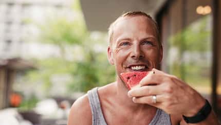 Ein Mann beißt glücklich in eine Wassermelone Ein Mann beißt glücklich in eine Wassermelone
