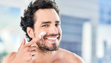 Ein Mann trägt lächelnd Sonnencreme im Gesicht auf Ein Mann trägt lächelnd Sonnencreme im Gesicht auf
