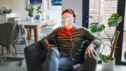 Ein Mann sitzt im Sessel mit einer LED-Maske fürs Gesicht Ein Mann sitzt im Sessel mit einer LED-Maske fürs Gesicht