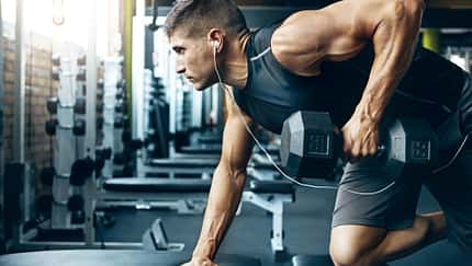 Ein trainierter Mann im Gym, der Rudern mit einer Kurzhantel an einer Bank macht