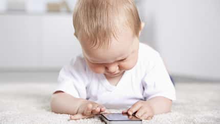 Ein Baby liegt auf dem Fußboden und spielt an einem Smartphone Ein Baby liegt auf dem Fußboden und spielt an einem Smartphone