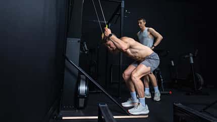 Zwei Männer trainieren im Fitnessstudio an einem SkiErgometer