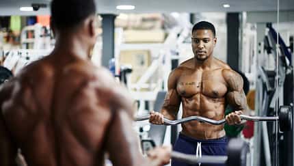 Ein muskulöser Mann trainiert mit einer Langhantel vor einem Spiegel im Fitnessstudio Ein muskulöser Mann trainiert mit einer Langhantel vor einem Spiegel im Fitnessstudio