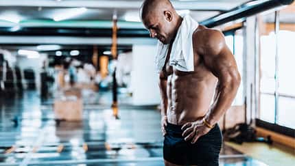 Trainierter Mann steht im Gym und schaut müde auf seinen Körper herab Trainierter Mann steht im Gym und schaut müde auf seinen Körper herab