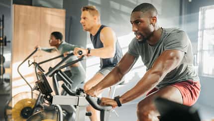 Zwei Männer und eine Frau trainieren im Gym auf dem Fahrrad Zwei Männer und eine Frau trainieren im Gym auf dem Fahrrad