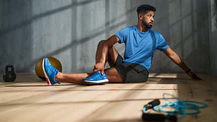 Ein Mann in blauem Sportoutfit stretcht sich vor einem grauen Hintergrund Ein Mann in blauem Sportoutfit stretcht sich vor einem grauen Hintergrund