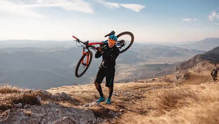 Mann trägt sein Mountain Bike auf einer Wanderung durch eine Berglandschaft