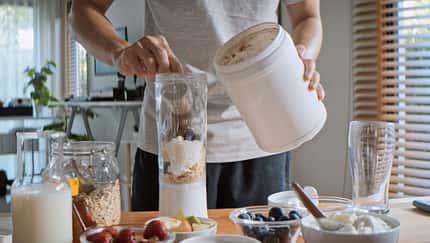 Ein junger Mann bereitet sich im Mixer einen Proteinshake zu Ein junger Mann bereitet sich im Mixer einen Proteinshake zu
