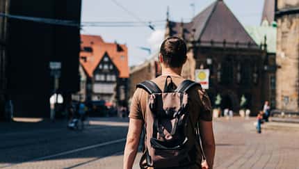 Ein junger Mann mit Rucksack spaziert durch die Straßen einer Altstadt Ein junger Mann mit Rucksack spaziert durch die Straßen einer Altstadt