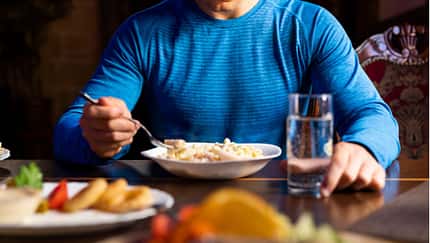 Nahaufnahme eines Mannes, der an einem reich gedeckten Tisch sitzt und Pasta isst Nahaufnahme eines Mannes, der an einem reich gedeckten Tisch sitzt und Pasta isst