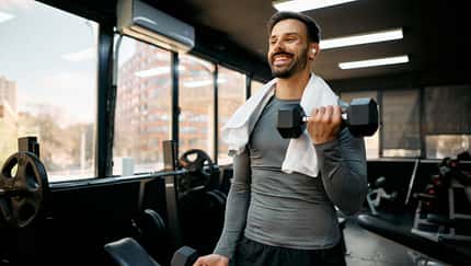 Junger Sportler, der mit Kurzhanteln im Fitnessstudio trainiert Junger Sportler, der mit Kurzhanteln im Fitnessstudio trainiert