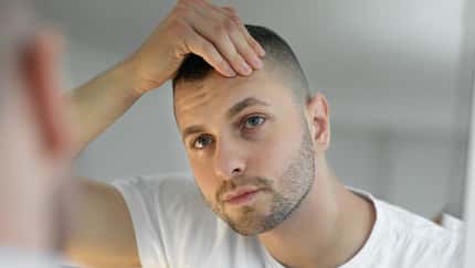 Ein junger Mann mustert sein Gesicht im Spiegel