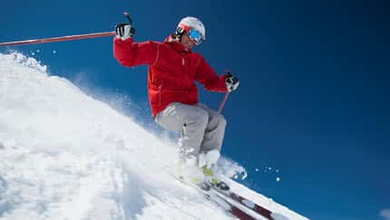 Ein Mann fährt bei blauem Himmel im Schnee eine Ski-Piste herunter Ein Mann fährt bei blauem Himmel im Schnee eine Ski-Piste herunter