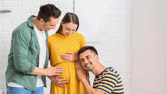 Zwei Männer kümmern sich um eine schwangere Frau