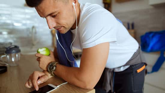 Junger Mann tippt mit Apfel und Sportkleidung auf sein Smartphone