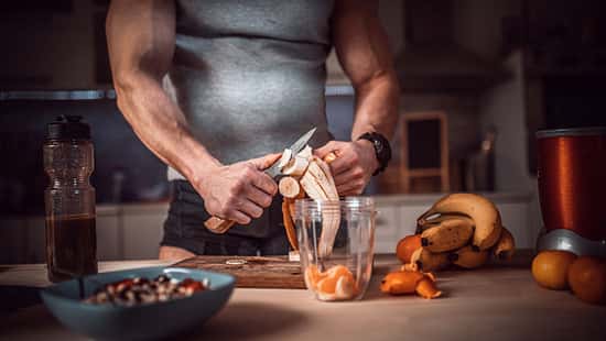 Ein trainierter Mann bereitet sich mit Obst einen Shake zu