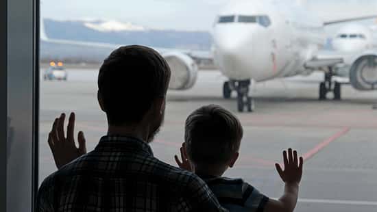 Ein Vater und sein Sohn stehen am Gate eines Flughafen und schauen sich die Flugzeuge an