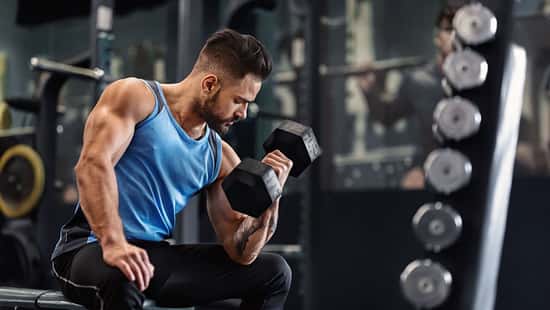 Bodybuilder,Pumping,His,Biceps,With,Dumbbell,In,Gym,,Empty,Space